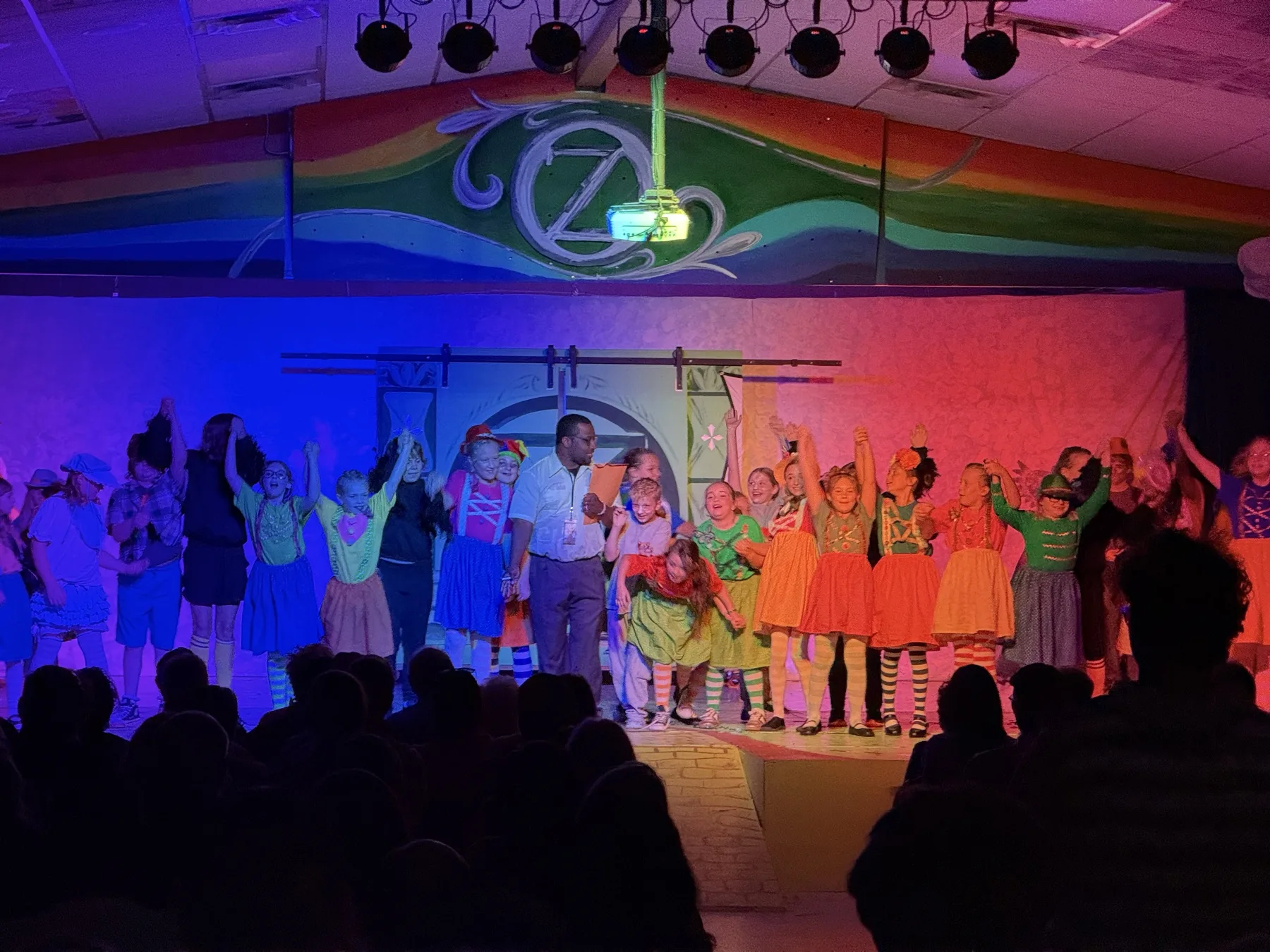 Jason Wright on stage with cast at Wizard of Oz finale, colorful rainbow backdrop